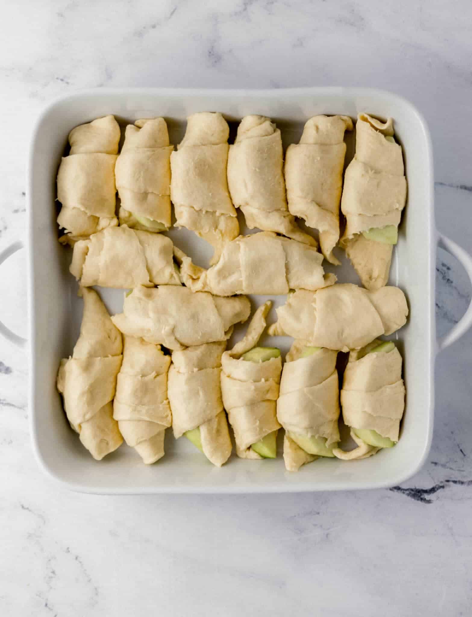apple slices wrapped in dough in white baking dish 