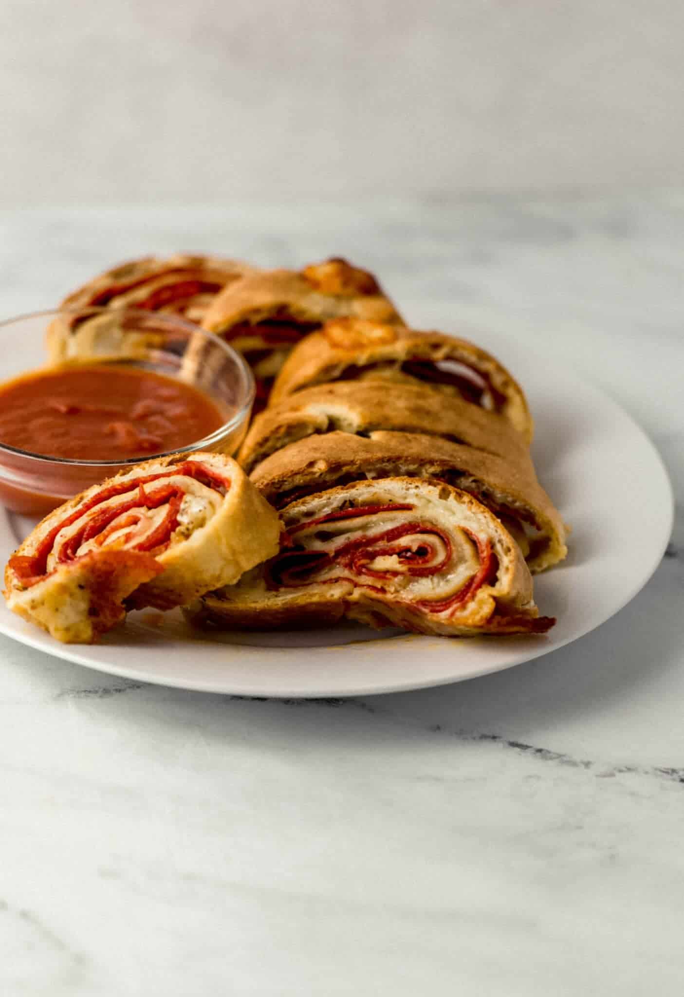 close up side view of sliced pepperoni bread on white plate with small bowl of sauce 