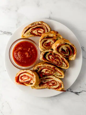 overhead view of finished pepperoni bread recipe on white plate in sliced with small glass bowl of dipping sauce