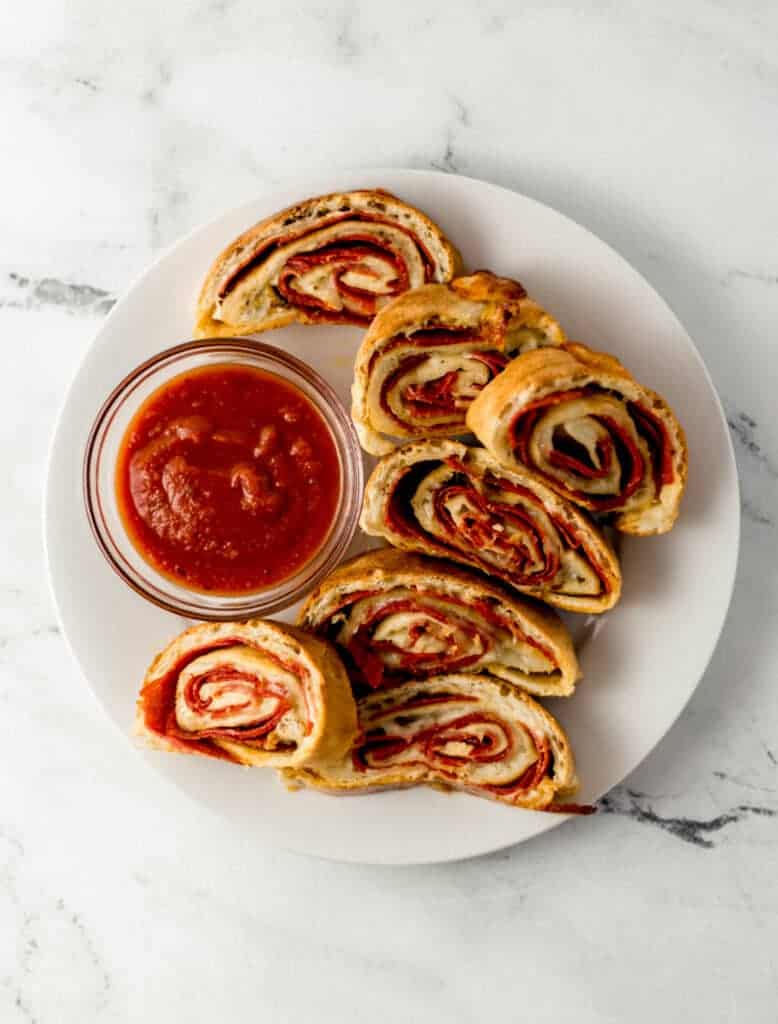 overhead view of finished pepperoni bread recipe on white plate in sliced with small glass bowl of dipping sauce