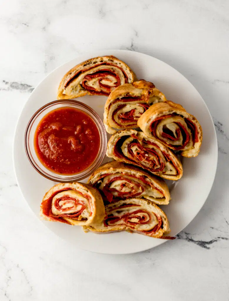overhead view of finished pepperoni bread recipe on white plate in sliced with small glass bowl of dipping sauce