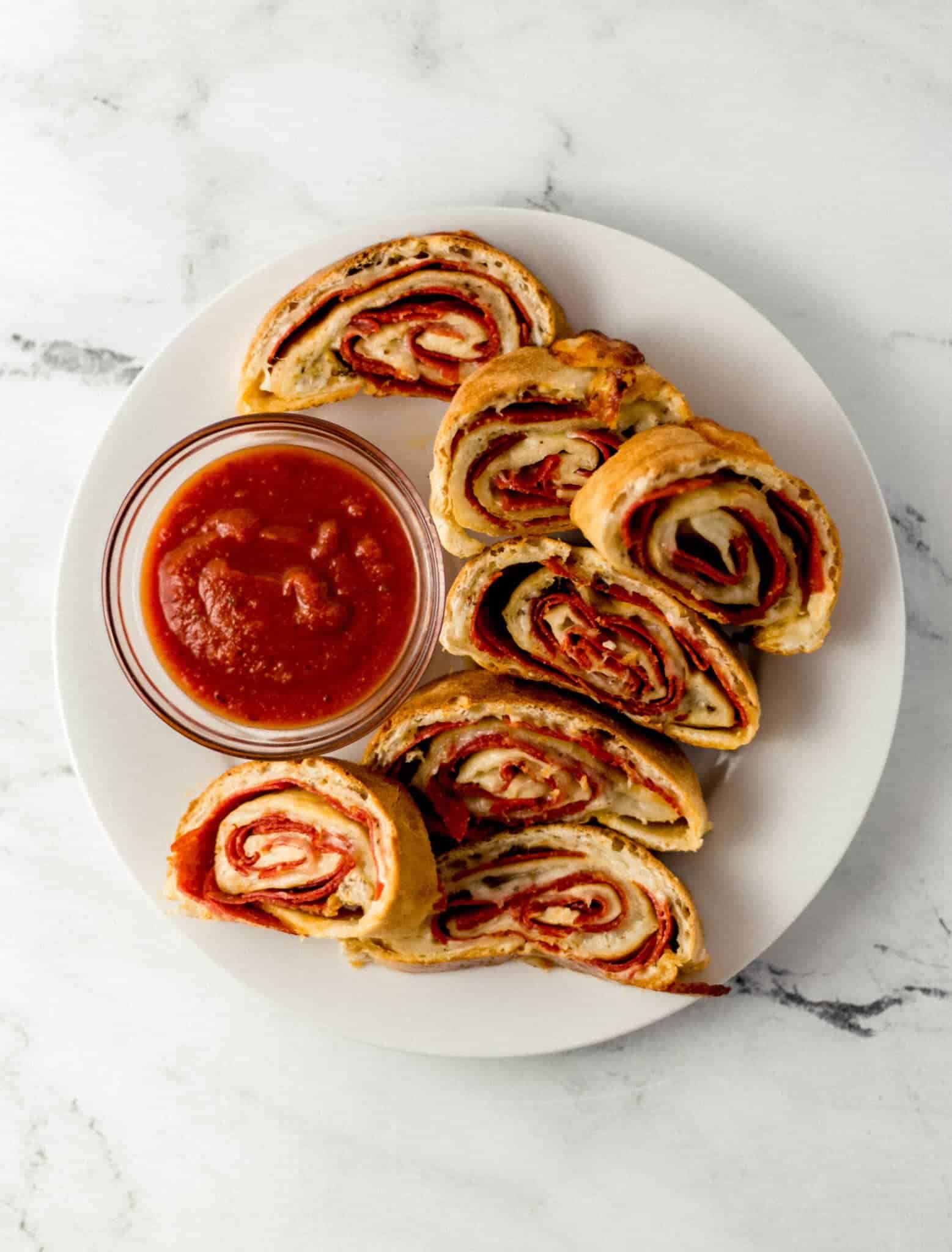 finished pepperoni bread on large white plate with small glass bowl of sauce