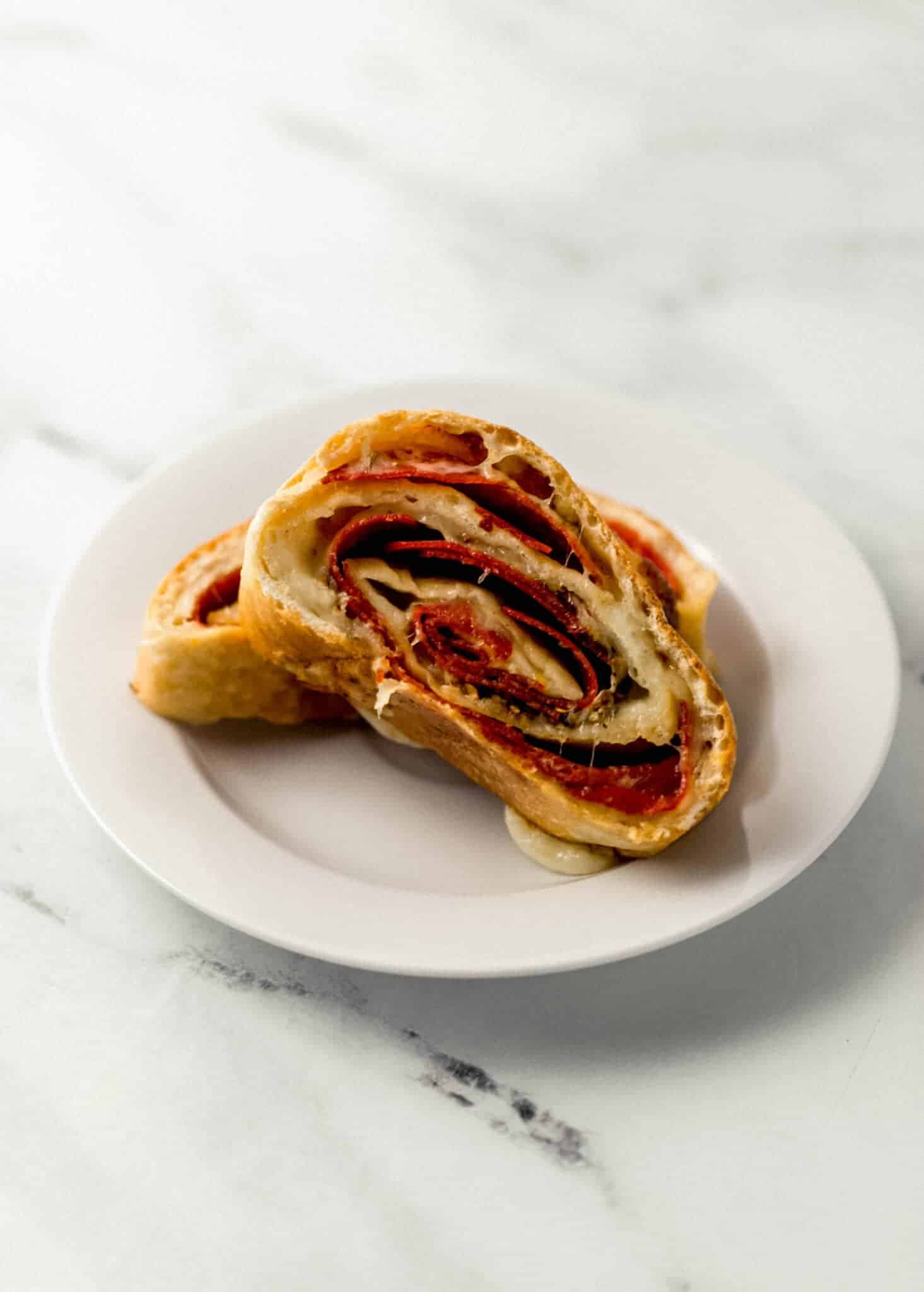 two sliced of finished pepperoni rolls on small white plate 