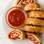 Overhead view of sliced bread on white plate with a small glass bowl of sauce.
