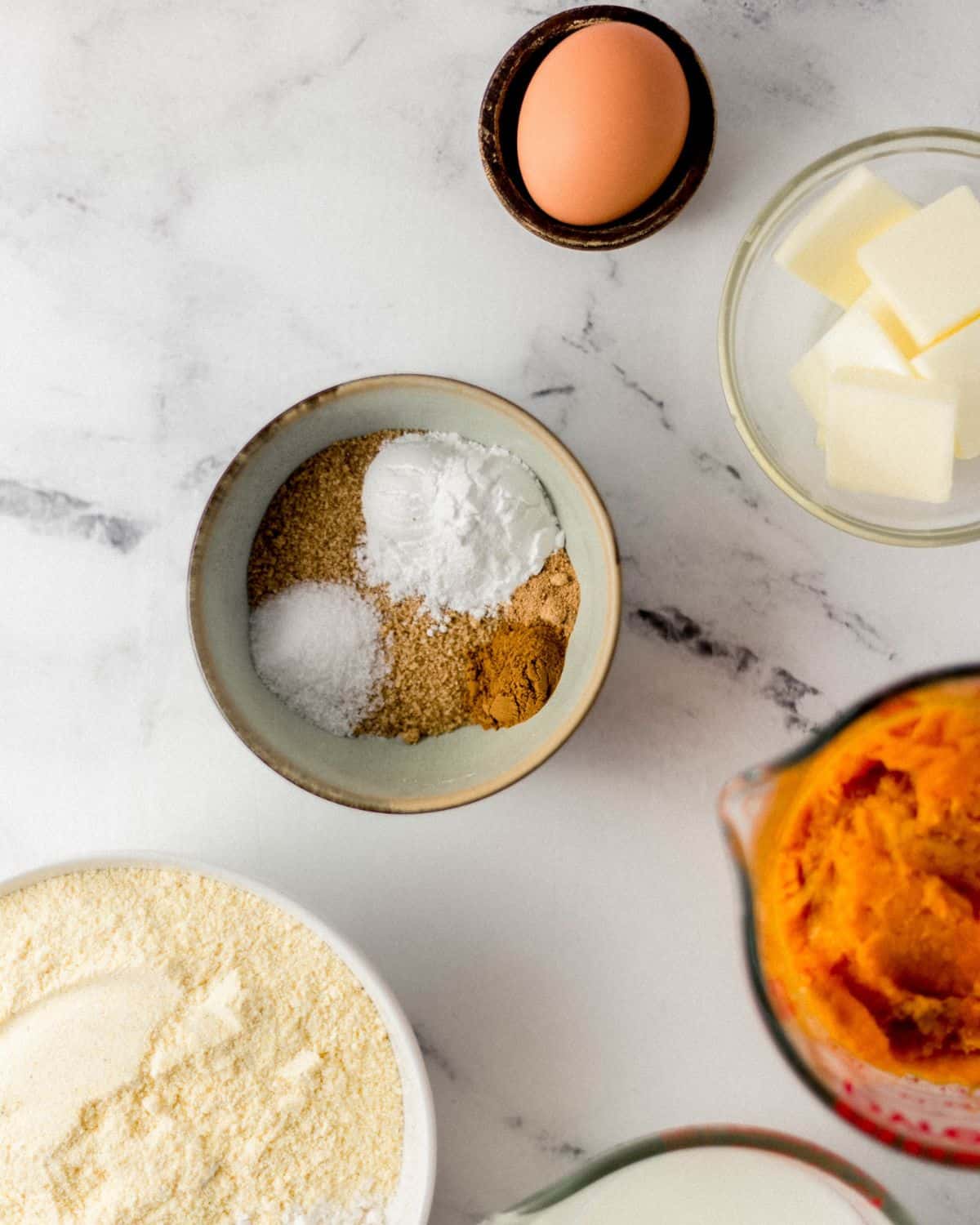 Ingredients needed to make cornbread in separate bowls on marble surface.
