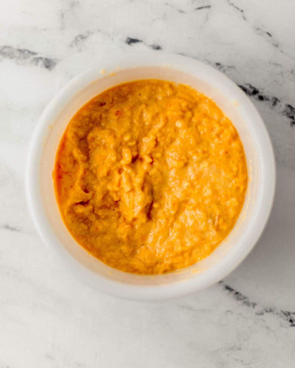 Wet ingredients to make cornbread in white bowl on marble surface.
