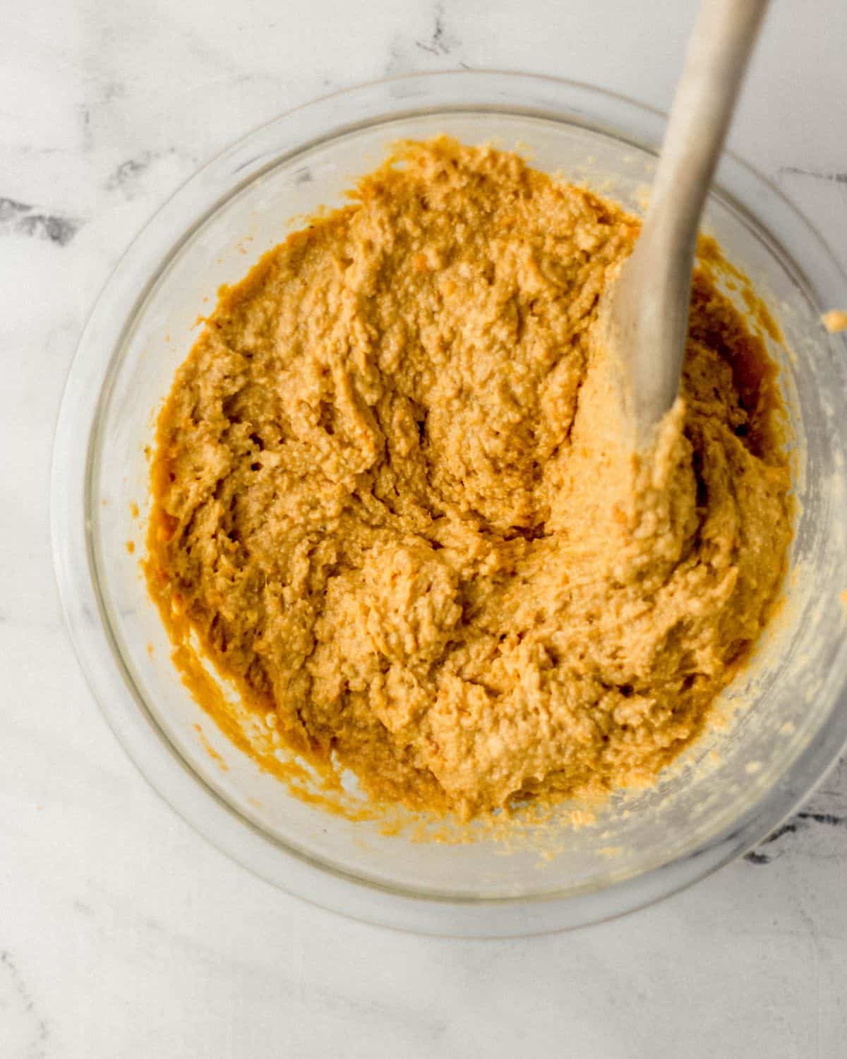 Overhead view of cornbread ingredients combined in glass bowl with wooden spoon.