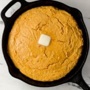 Overhead view of finished sweet potato cornbread in cast iron skillet topped with butter.
