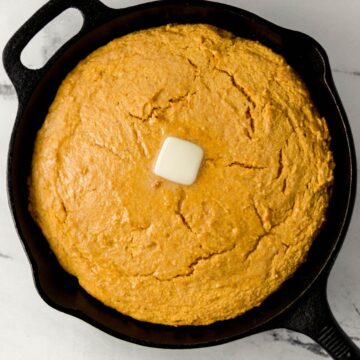 Overhead view of finished sweet potato cornbread in cast iron skillet topped with butter.