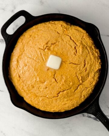 Overhead view of finished sweet potato cornbread in cast iron skillet topped with butter.