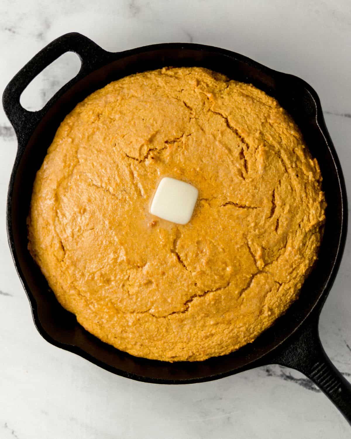 Overhead view of finished cornbread in cast iron skillet topped with butter.