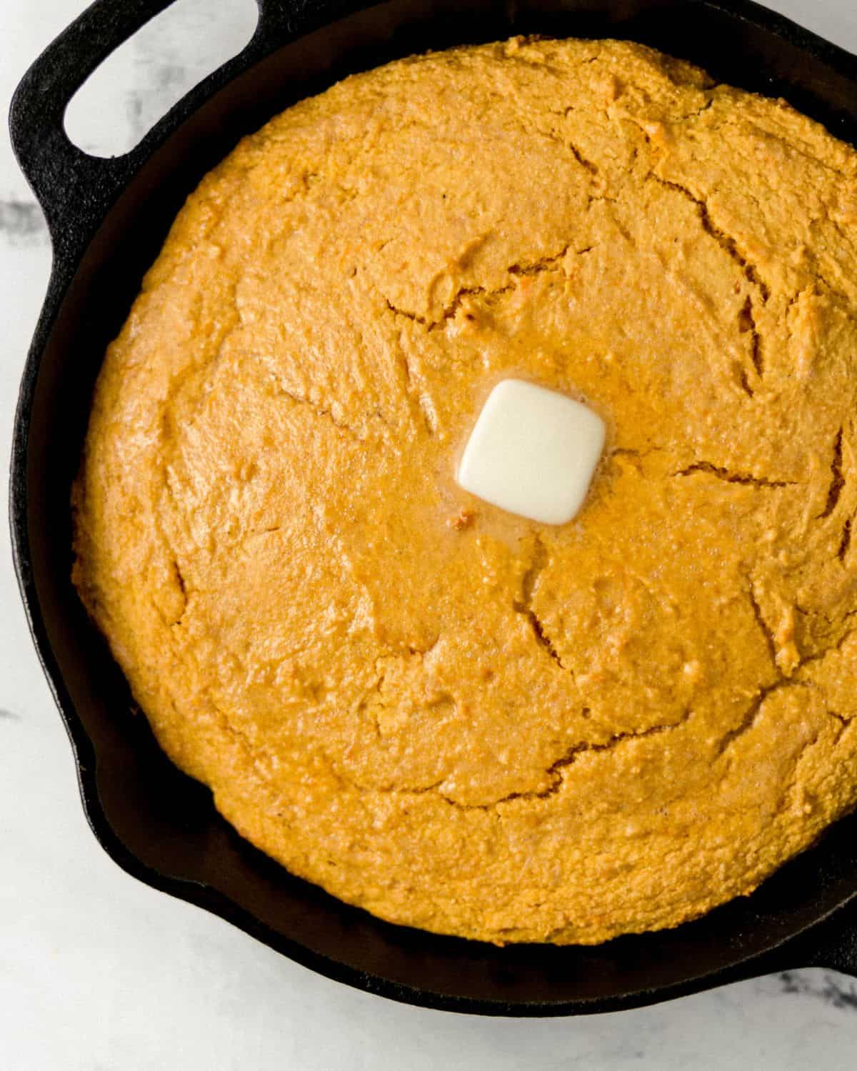 Overhead view of sweet potato cornbread in cast iron skillet topped with some butter.
