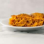 Close up side view of piece of cornbread on white plate.