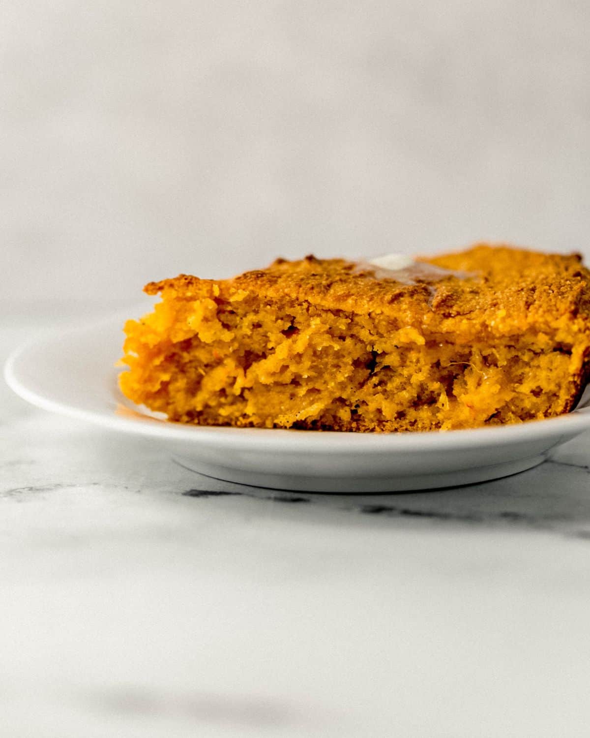 Close up side view of slice of cornbread on white plate.