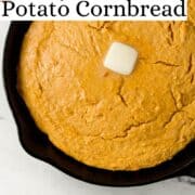 Close up view of baked cornbread in cast iron skillet topped with butter on pin with text overlay.
