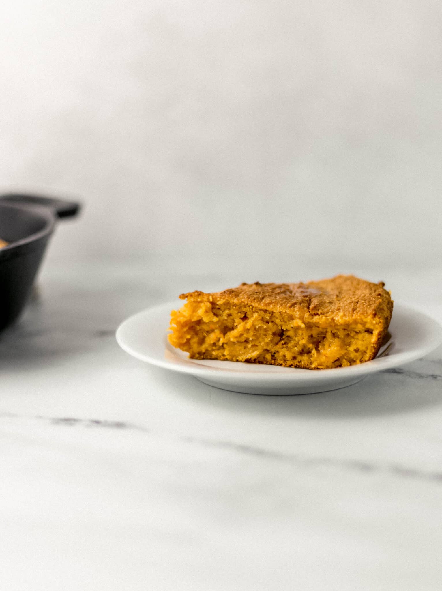 close up side view of a slice of cornbread on a white plate