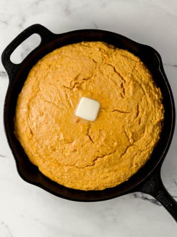 overhead view of sweet potato cornbread topped with butter in cast iron skillet
