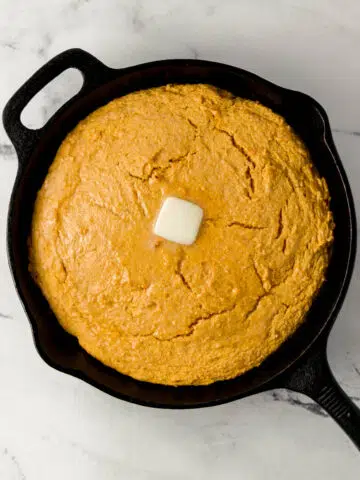 overhead view of sweet potato cornbread topped with butter in cast iron skillet