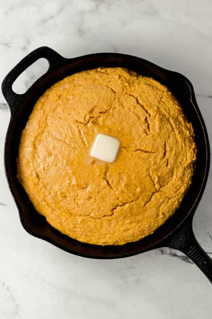 overhead view of sweet potato cornbread topped with butter in cast iron skillet