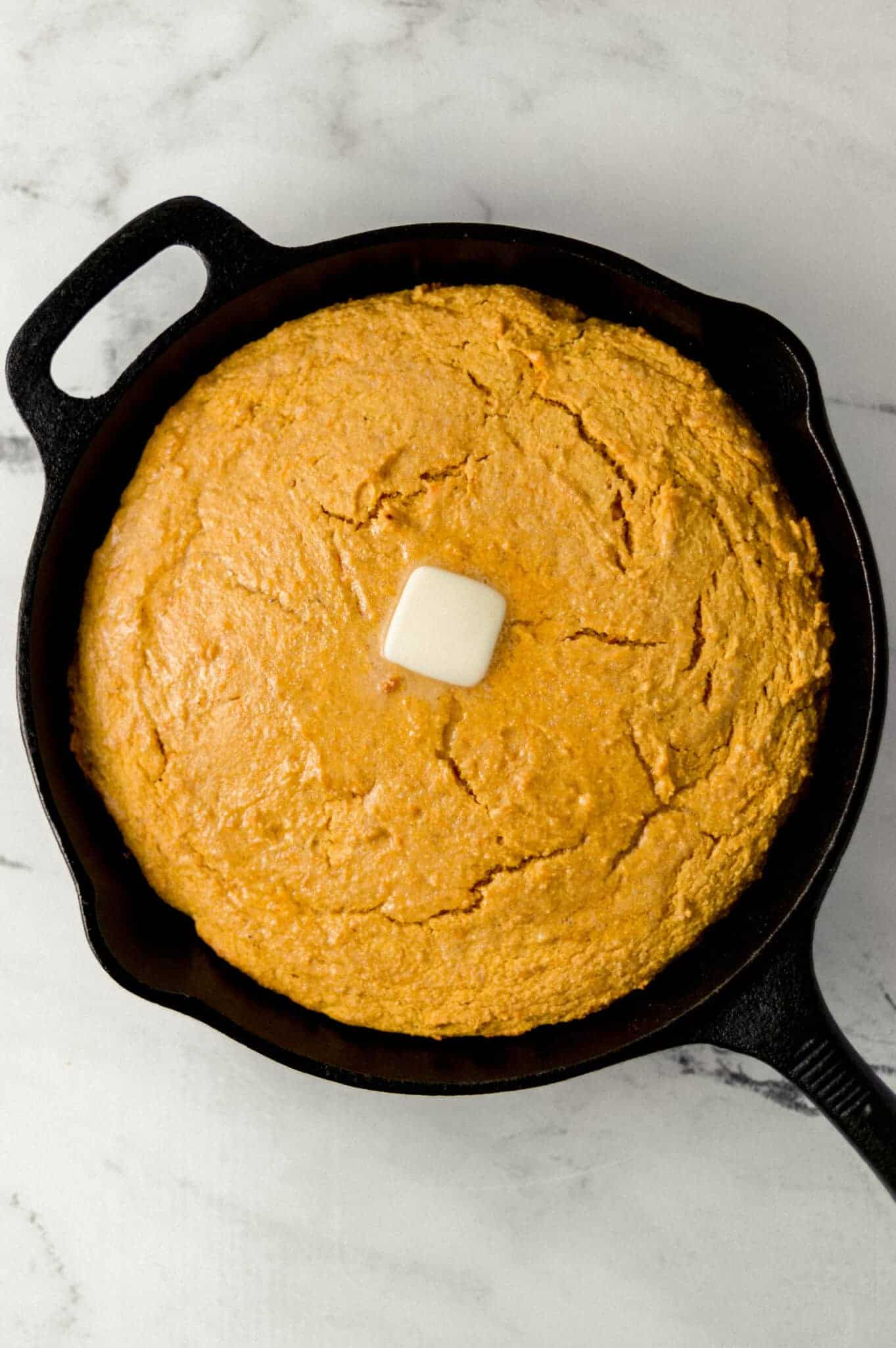 overhead view of finished cornbread topped with butter in cast iron skillet