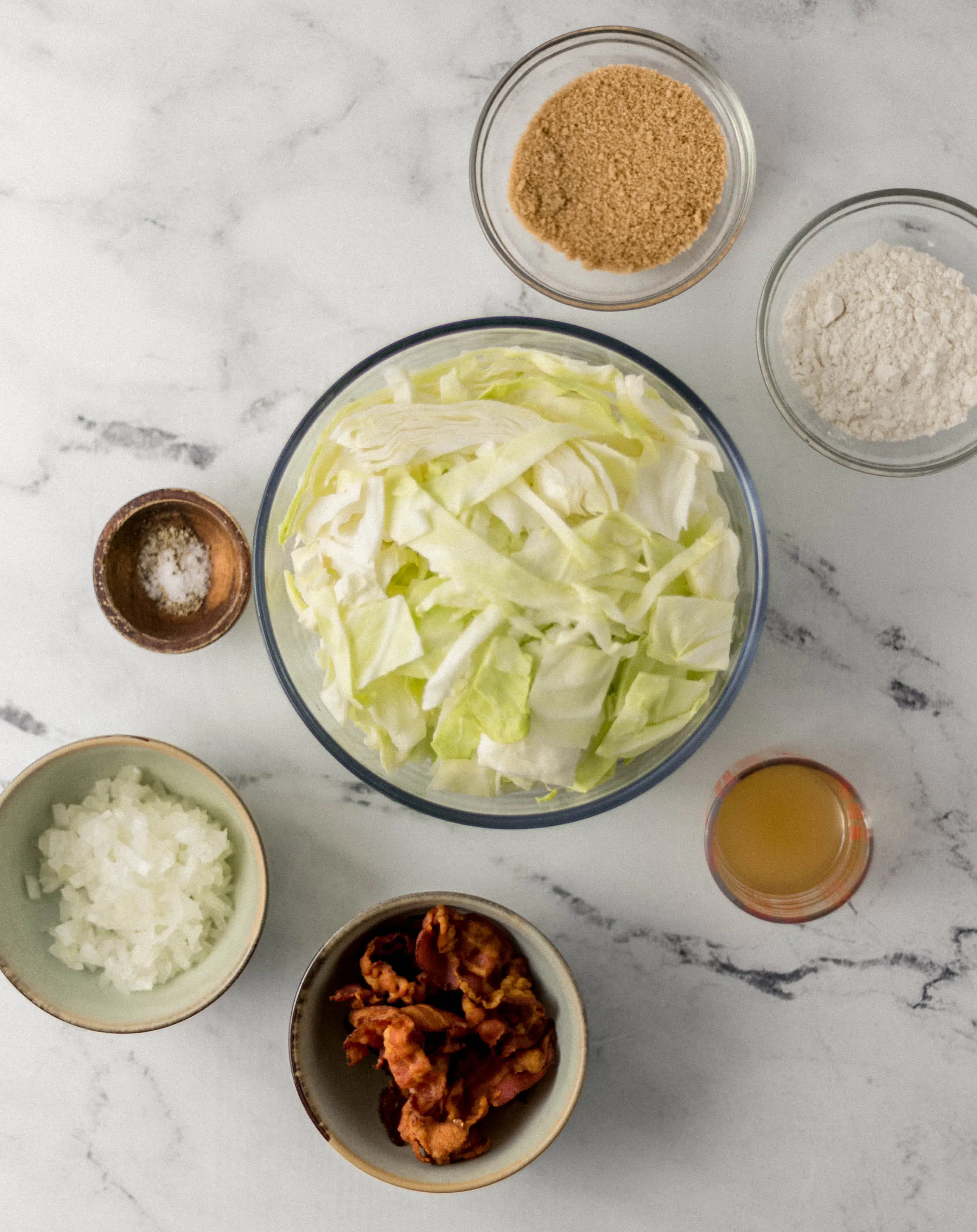 ingredients needed to make cabbage in separate bowls on marble surface 