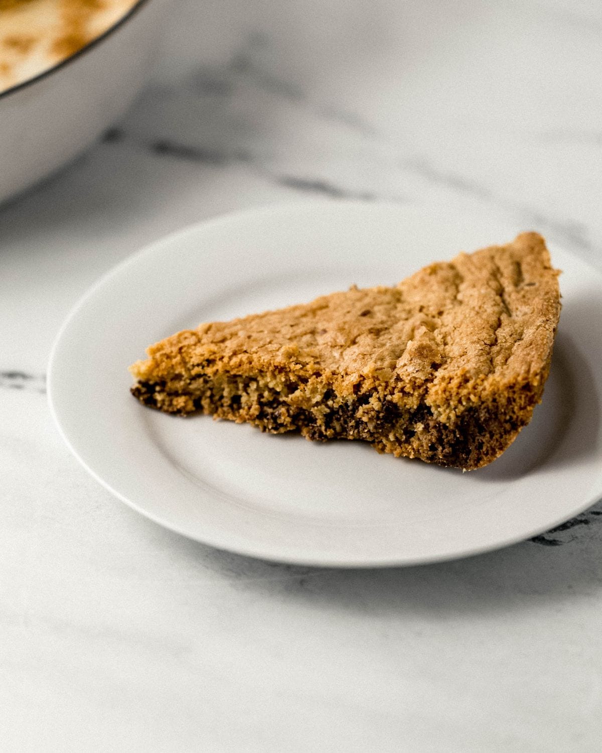 Chocolate Chip Cookie Skillet Close up side view of slice of cookie on white plate.