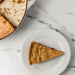 overhead view of piece of cookie on small white plate beside the rest of the cookie in the skillet