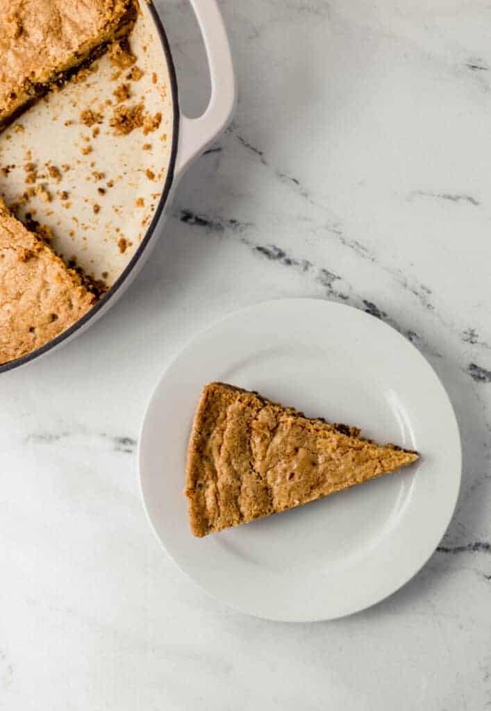 overhead view of piece of cookie on small white plate beside the rest of the cookie in the skillet