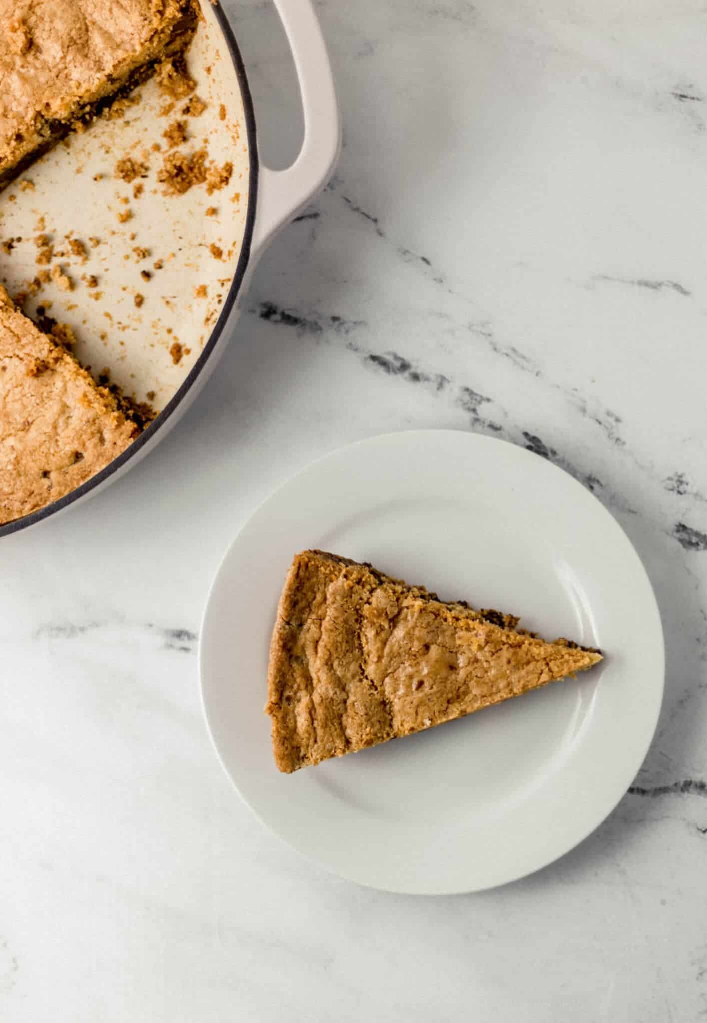 overhead view of skillet cookie and a piece of it cut out and on a white plate
