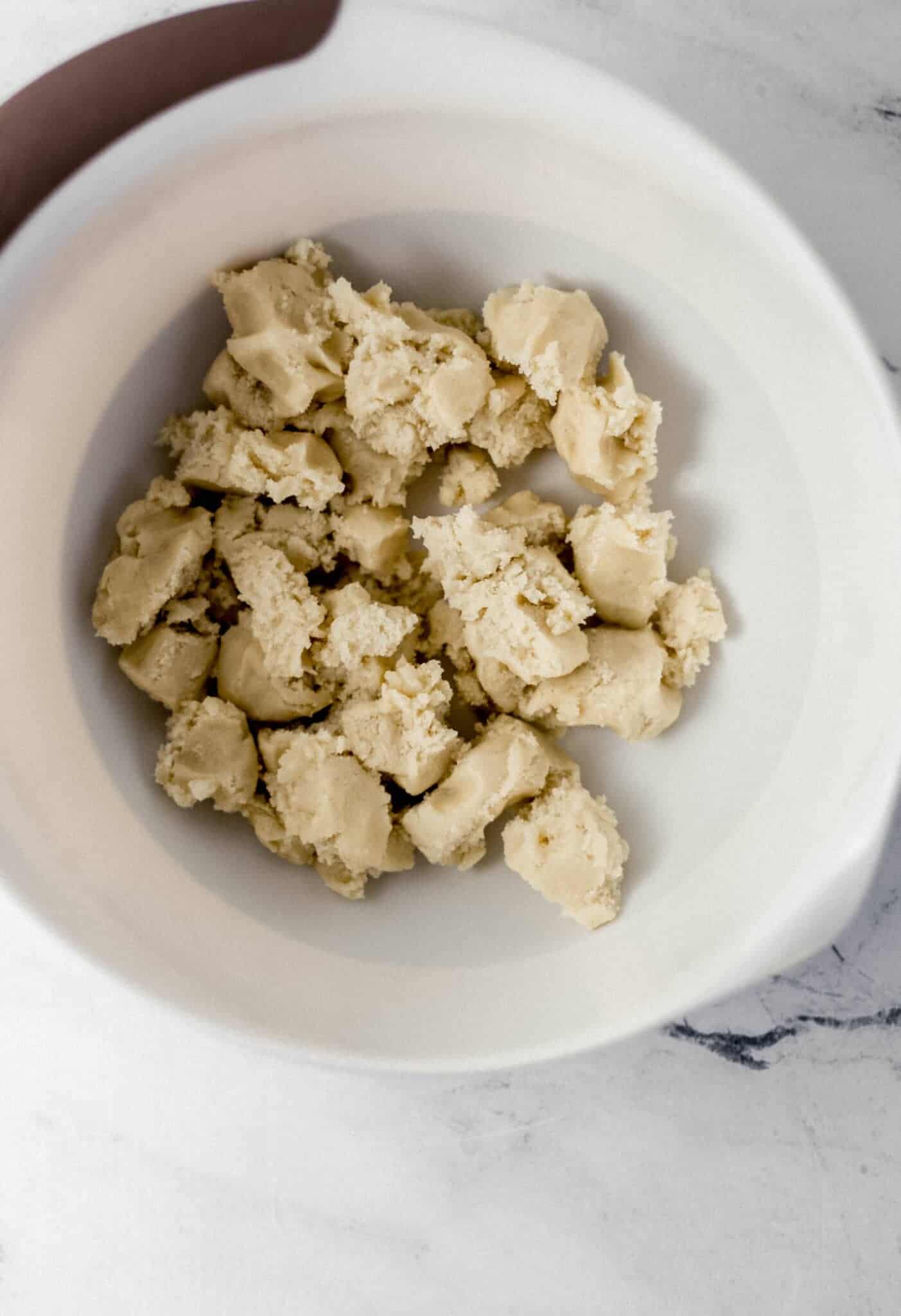 cookie dough broken up into chunks in a large white mixing bowl 