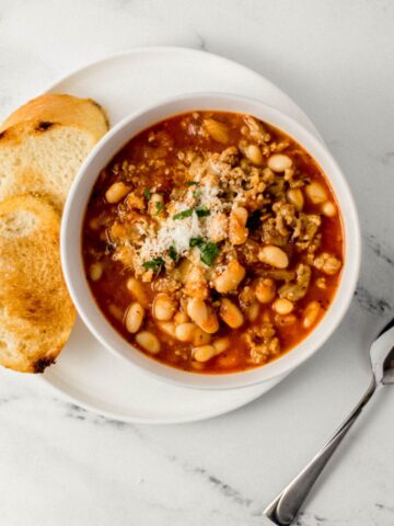 overhead view of bowl of finished soup over a plate with bread beside a spoon