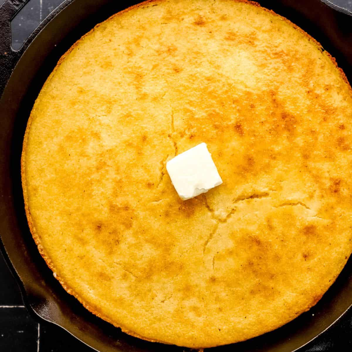 Close up view of finished southern cornbread in cast iron skillet topped with butter.
