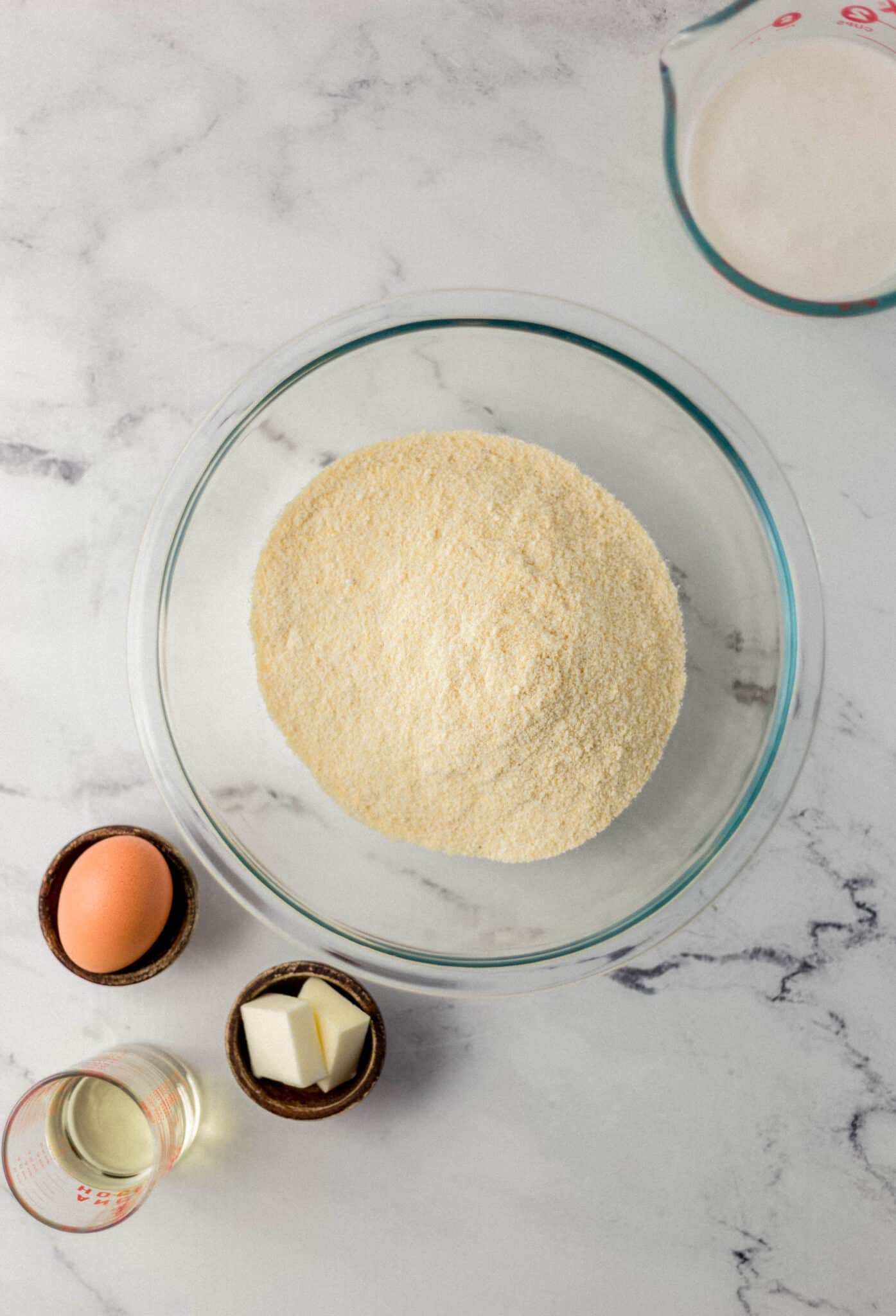 ingredients needed to make cornbread in separate containers on marble surface 