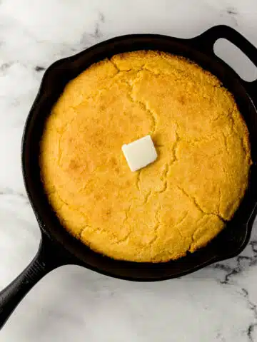 overhead view of finished cornbread in cast iron skillet topped with butter
