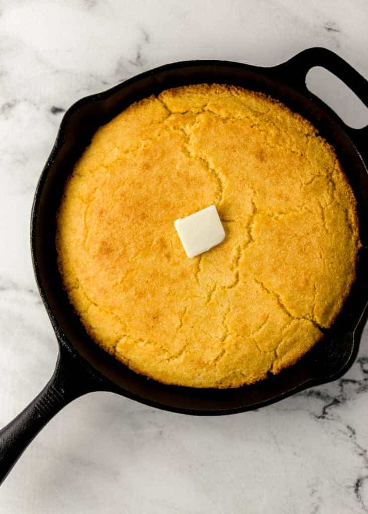 overhead view of finished cornbread in cast iron skillet topped with butter