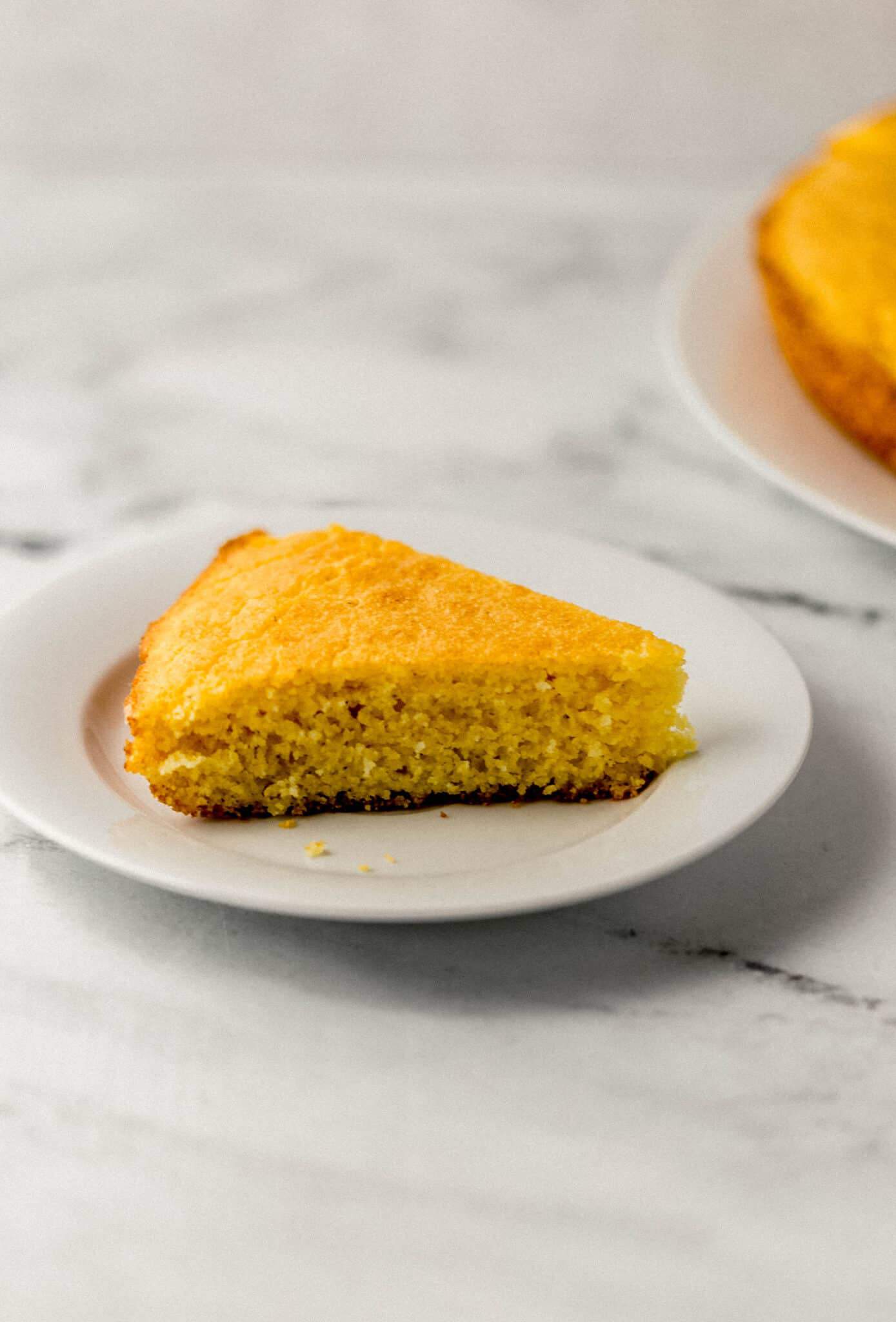 close up side view of piece of cornbread on white plate 