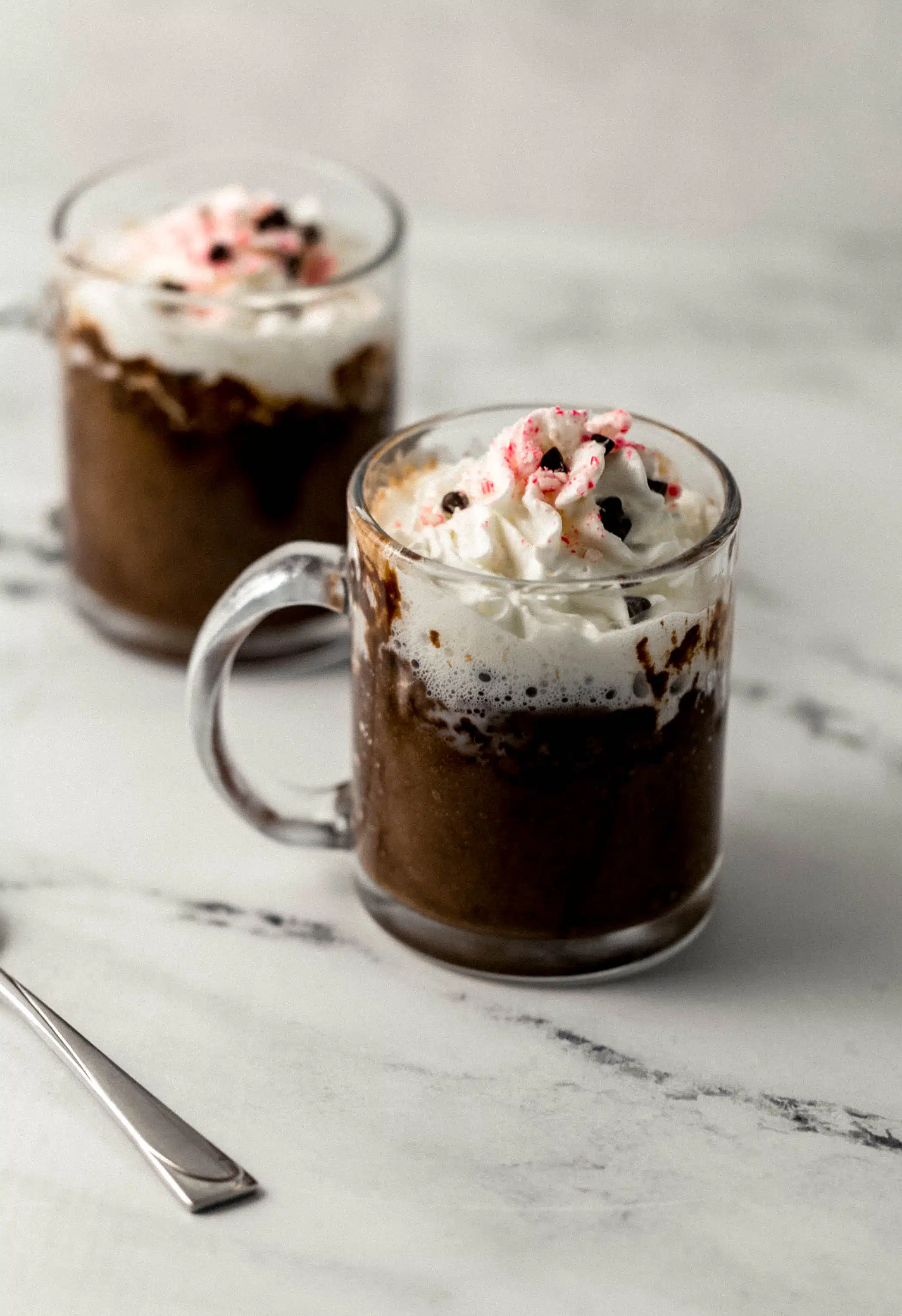 two finished mug cakes topped with whipped cream, peppermint, and chocolate chips