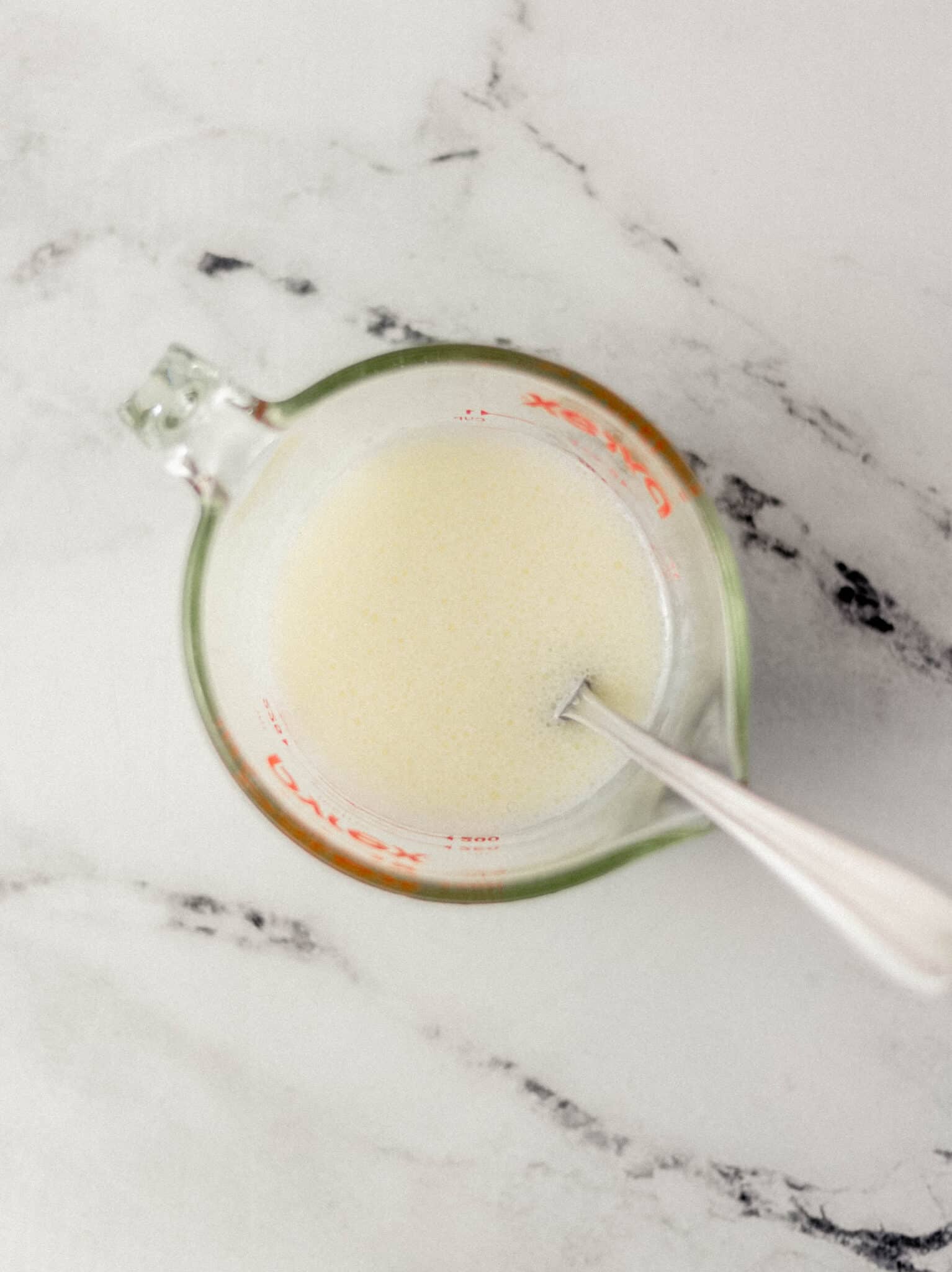 milk and oil combined in glass measuring cup with spoon