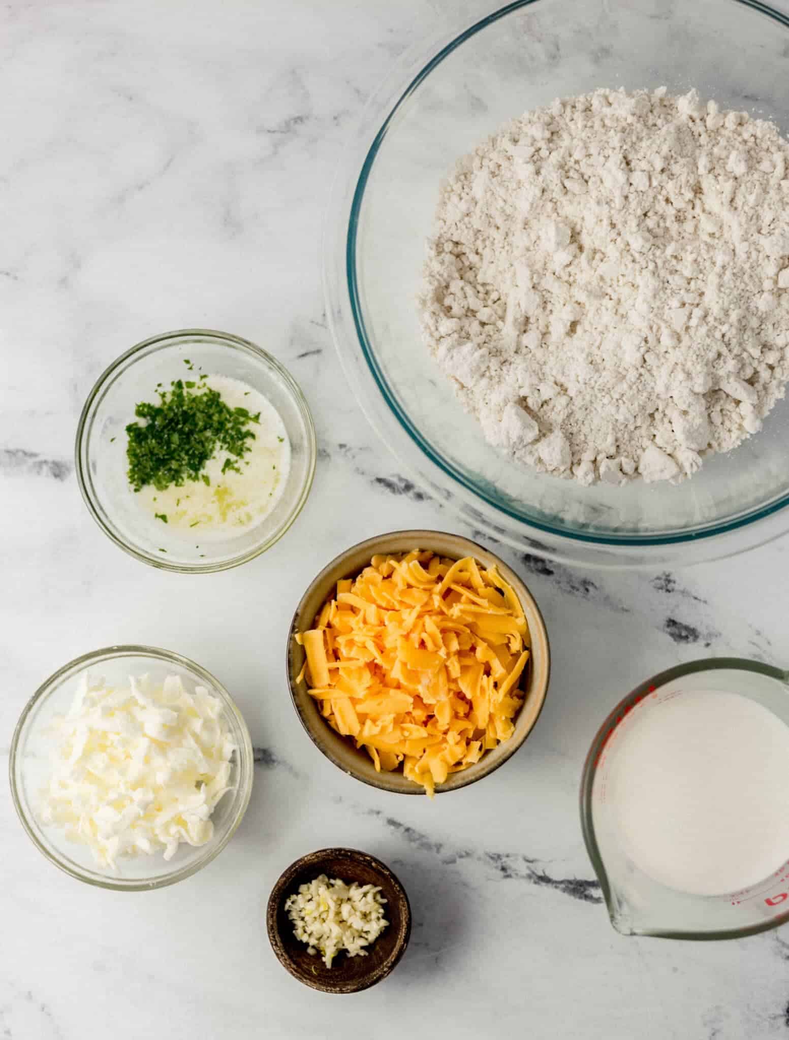 ingredients needed to make biscuits in separate bowls on marble surface 