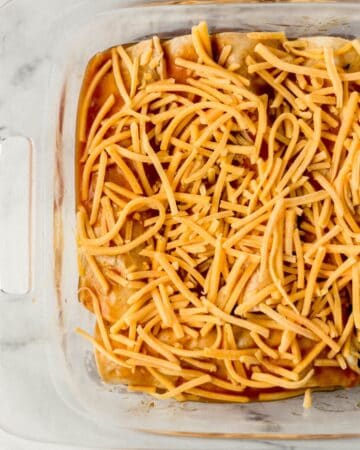 Enchiladas topped with shredded cheese in baking dish.
