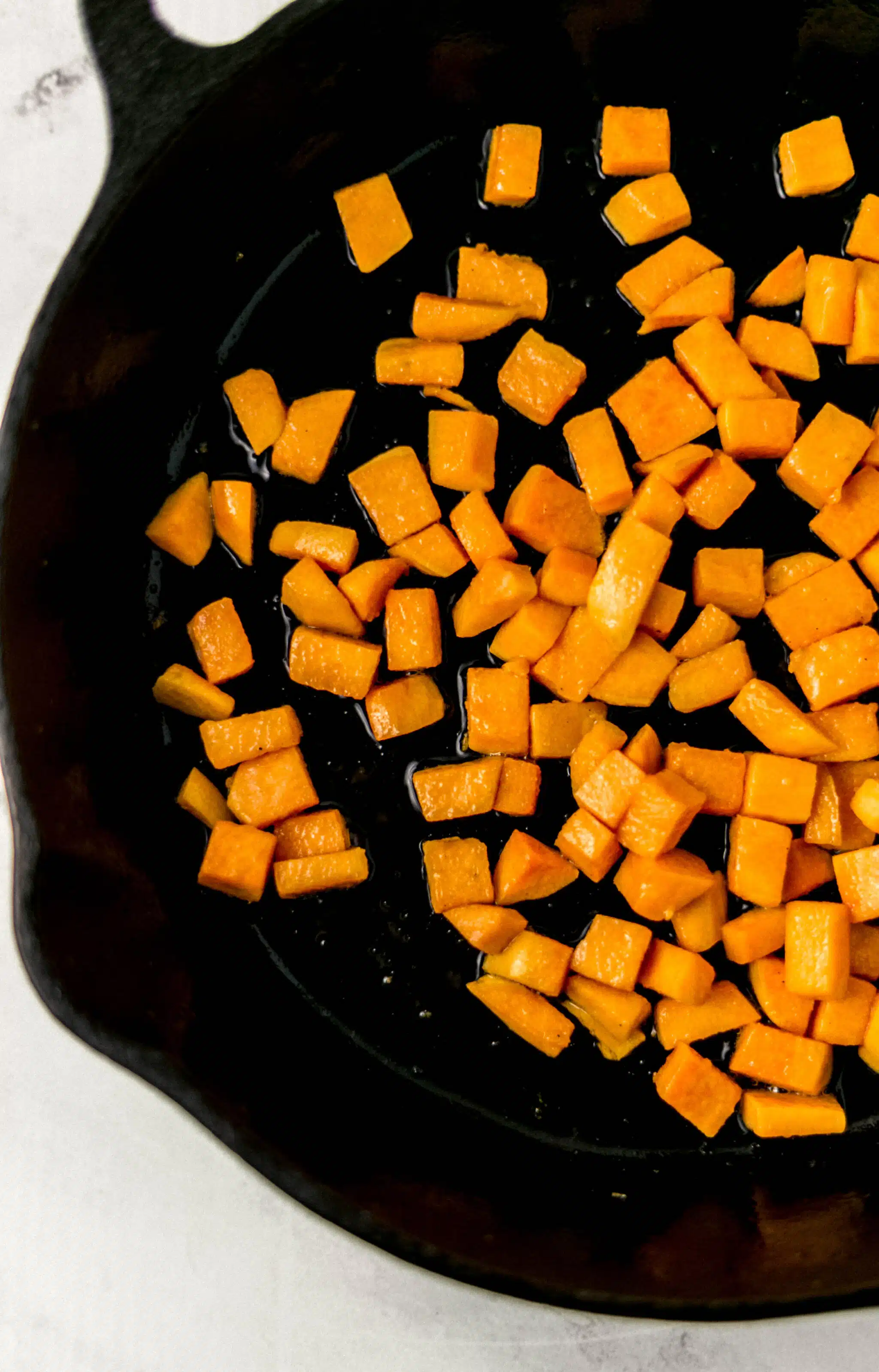 cubed sweet potato in cast iron skillet with oil and salt 