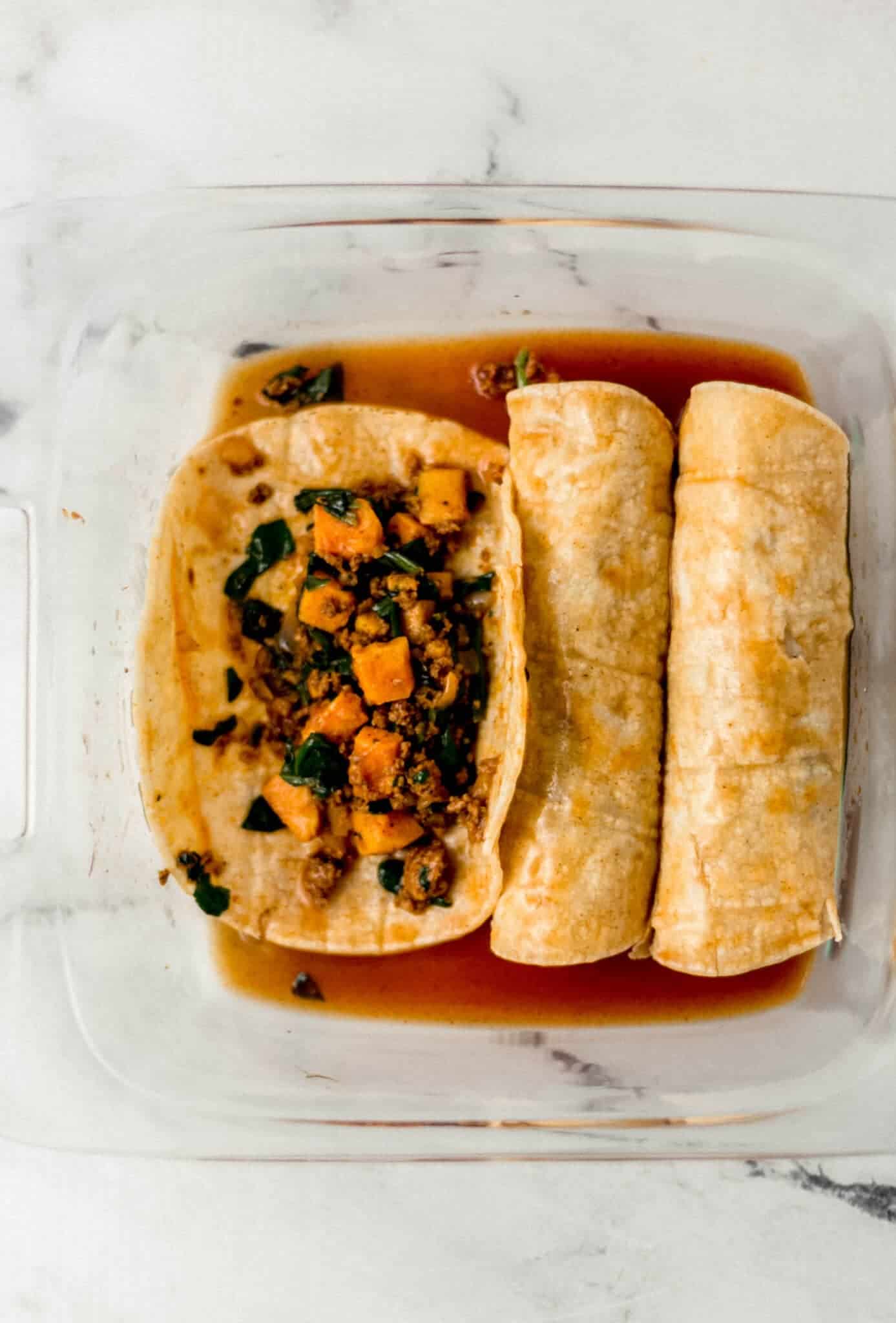 filling added to tortillas and sauce in square glass baking dish 