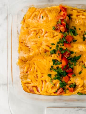 overhead view of enchiladas topped with chopped spinach and tomatoes