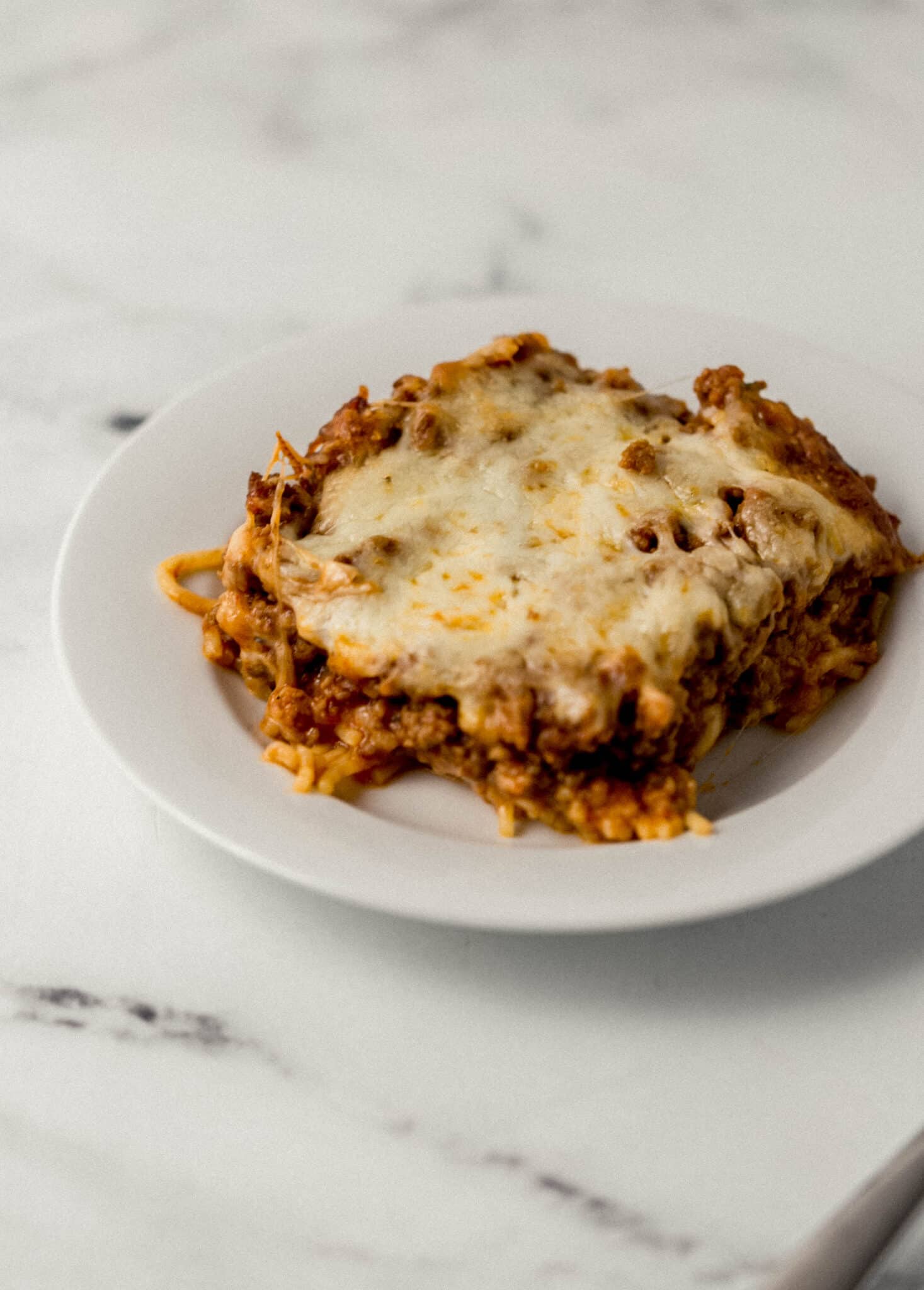 close up side view of single serving of baked spaghetti on white plate