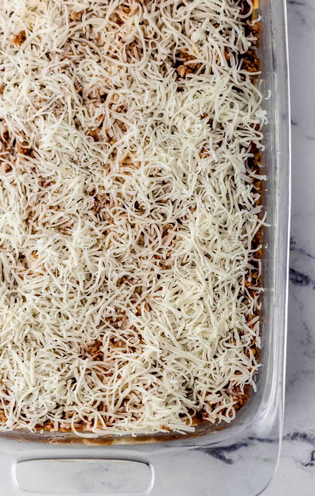 spaghetti topped with meat sauce and more shredded mozzarella cheese in glass baking dish 