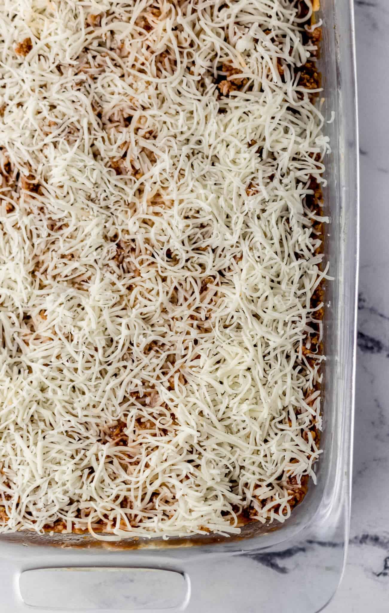 spaghetti topped with meat sauce and more shredded mozzarella cheese in glass baking dish