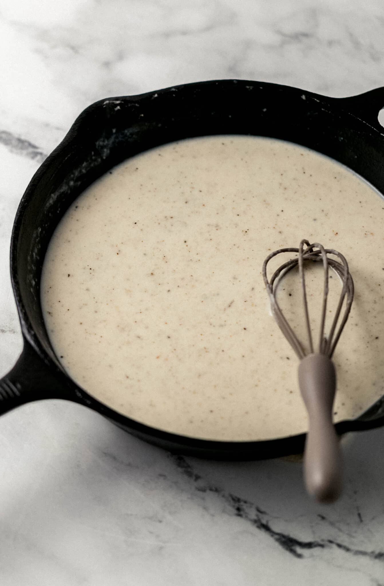 milk, bacon dripping, seasoning, and flour combined in cast iron skillet with whisk