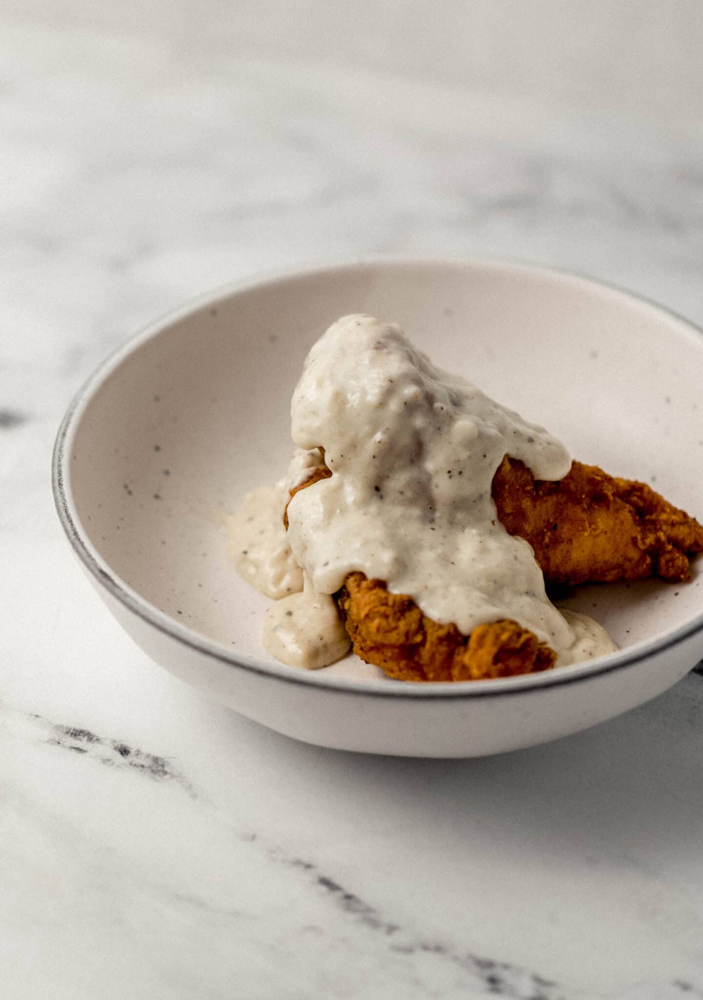 gravy on top of chicken tenders in white bowl 