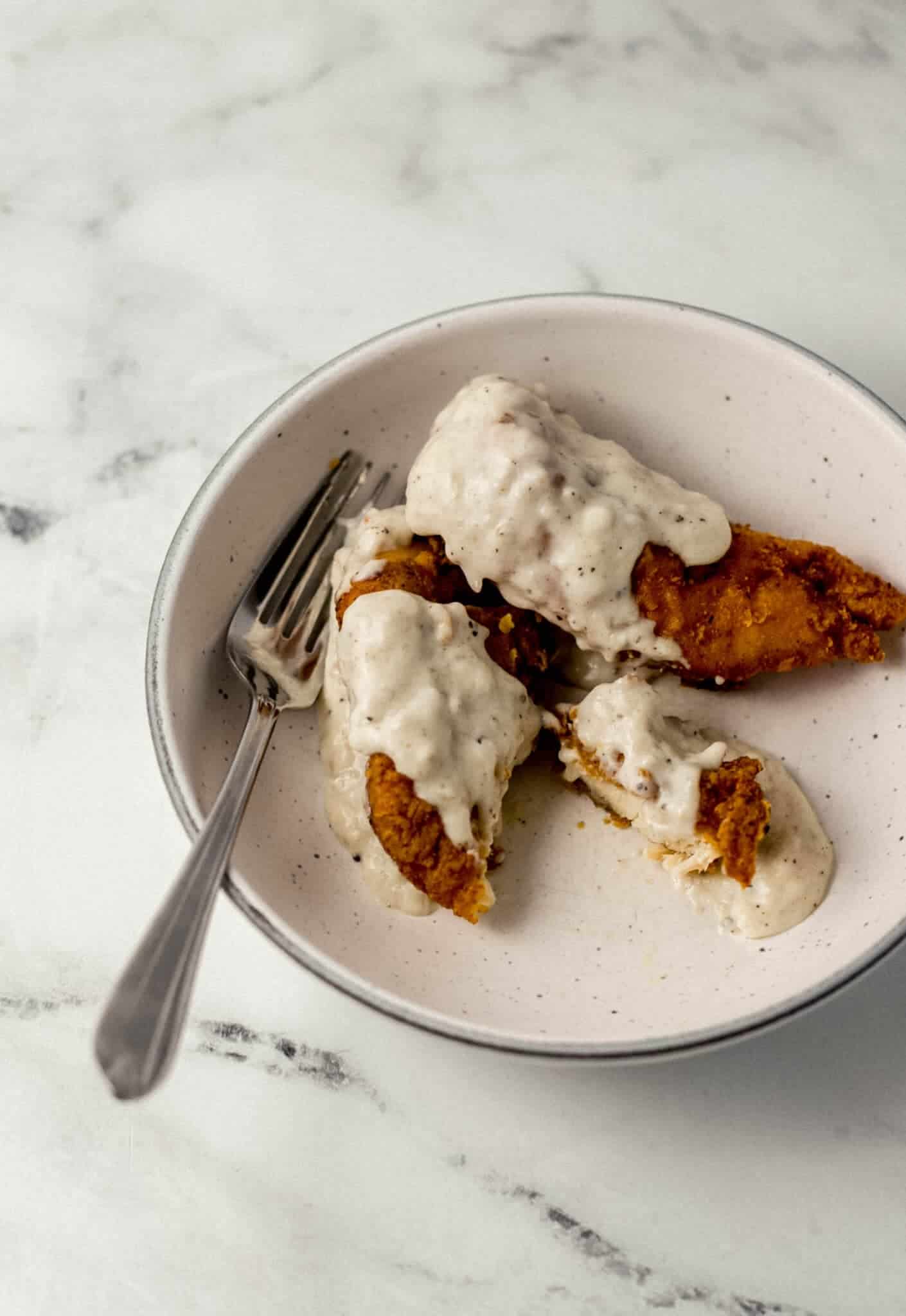 chicken tender, gravy, and a fork in a white bowl