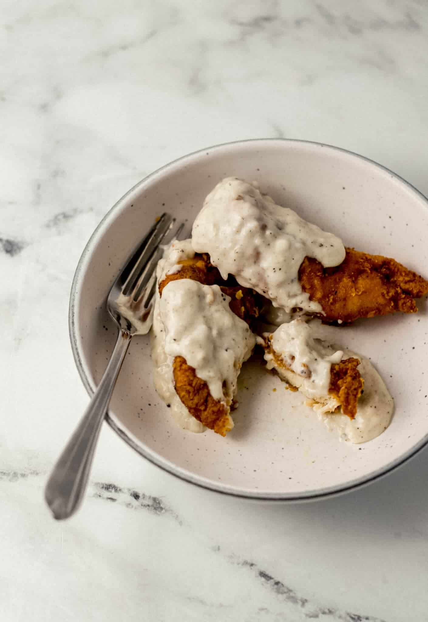 chicken tender, gravy, and a fork in a white bowl 